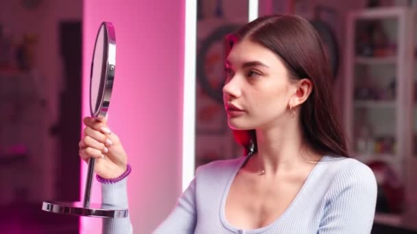 Beautiful girl with perfect skin face looks herself in mirror in beauty salon — Stock Video