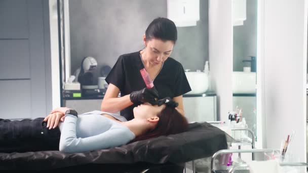 Maestro hace permanente el procedimiento de maquillaje de cejas a la mujer en el salón de belleza. — Vídeo de stock