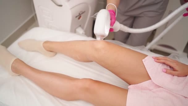 Делает удаление волос на ногах женщине, которая лежит на медицинском диване — стоковое видео