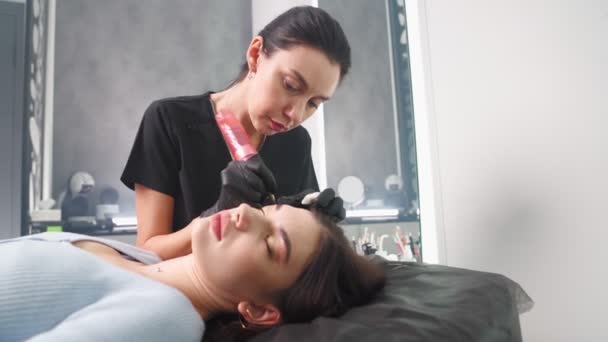 Maestro hace permanente el procedimiento de maquillaje de cejas a la mujer en el salón de belleza. — Vídeos de Stock