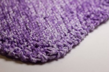 Bu resim, mor ve beyaz tonlarında, jartiyer dikişinde el örgüsü iplik kumaşının makro soyut bir arkaplanını gösteriyor..