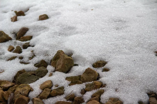 この画像は コピースペースで 日焼け色砕いた造園岩を覆う白い雪の抽象的なテクスチャの背景を示しています — ストック写真