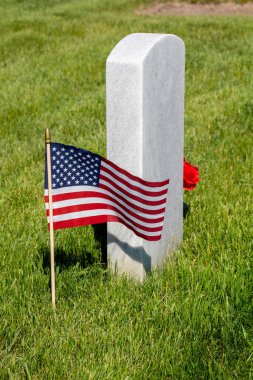 Amerikan bayrağı ve basit bir buket çiçekle süslenmiş tek bir askeri mezar taşına yakından bakın.