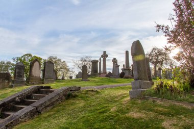 Upward hillside view of old gravestones in a European cemetery at dusk, with lens flare
