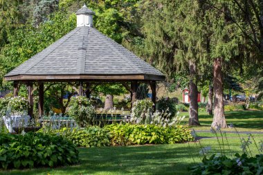 Güzel, koyu kahverengi, ahşap bir çardağın peyzajı, bir parkın peyzajı ile çevrili.