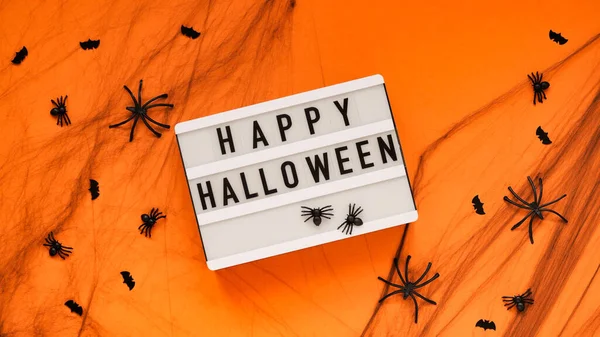 White board for text with the word Happy Halloween,bats and spiders in a spider\'s web on a orange background, top view, flat lay. Concept card for the holiday of the dead, Halloween