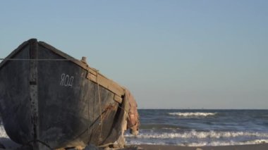 Eski ahşap bir balıkçı teknesinin güneş batarken fırtınalı denizin dalgalarına karşı kumlu deniz kıyısında demirlemiş halatı. Deniz manzarası, güzel 4K videosu. Rüzgarlı hava.