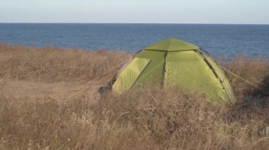 Kapalı yeşil çadır kamp kumsalı, kuru çayır ya da çimenler rüzgarda salınan çadır ve deniz zeminine karşı okyanus. Sahilde çadırlarda tatil, aktif yaşam tarzı. Çadırlarla seyahat edin.