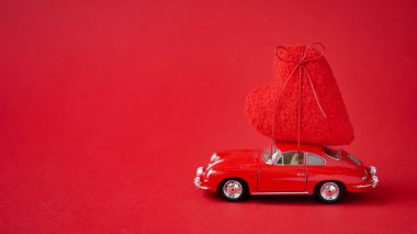 Kırmızı arka planda, çatıda büyük yumuşak bir hediye şeklinde kırmızı bir araba. Sevgililer Günü veya düğün günü romantik bir gezi anlayışı. Güzel bir tatil kartı..