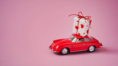 Çatıda pembe arka planda hediye kutusu olan kırmızı araba, kopyalama alanı. Sevgililer Günü 'nde ya da düğün gününde romantik seyahat kavramı. Güzel bir tatil kartı. Aşk.