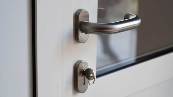 Close-up of a metal key in the keyhole in a plastic white door, the front door to the office, house, apartment. Modern interior, front door handle. Business