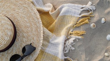 Yakın çekim hasır şapka, güneş gözlüğü ve sarı kareli plaj ekoseli deniz kabuklarına karşı kum yatar, üst manzara, düz döşeme, kopyalama alanı. Yaz tatili afişi, seyahat, sahil beldesi, dinlenme plajı
