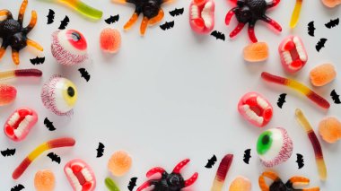 Beyaz zemin üzerinde, parlak jöle şekerlemeleri, örümcekler, gözler, çeneler, solucanlar ve yarasalar, beyaz arka plan, üst görünüm, düzlük, kopya alanı. Cadılar Bayramı partisi için dekor konsepti, bayram ziyafeti, abur cubur. Desen