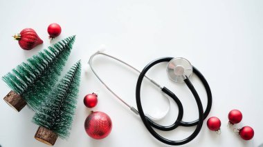 Noel medikal afişi. Hediye kutusunu, köknar dallarını, konileri, köknar ağaçlarını, kırmızı topları ve steteskopu beyaz arka planda, üst tarafta, düz yerde, kopyalama alanında kapatın. Yeni yıl tıbbı, doktor için tebrikler.