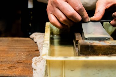 Usta bir kılıç ustası Japonya 'da bir taşın üzerinde bir bıçağı keskinleştiriyor..