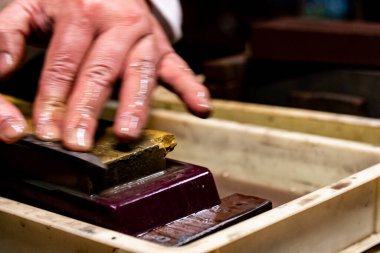 Usta bir kılıç ustası Japonya 'da bir taşın üzerinde bir bıçağı keskinleştiriyor..