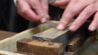Master swordsmith is sharpening knife on grindstone with water
