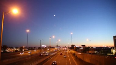 Busy traffic on a highway under the moon and blue and orange sunset sky in Toronto, Ontario, Canada. 