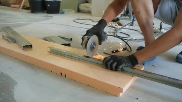 Een man met een slijpmachine snijdt een metalen profiel af. close-up. Vonken vliegen weg. Concept - renovatie appartement DIY. — Stockvideo