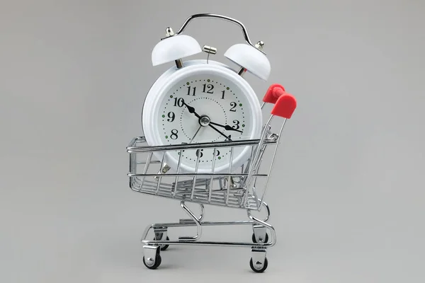 Gri bir arka planda süpermarket tramvayındaki beyaz saat. Konsept - zaman kazanmak, online mağazalardan mal almak, teslimatla birlikte. Salgın sırasında güvenli, uzak bir alışveriş.