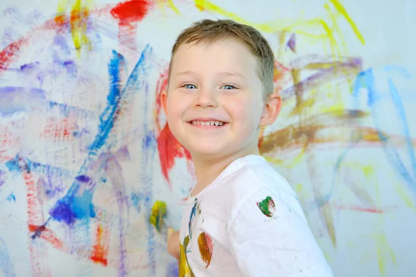 Красивый голубоглазый мальчик смотрит в камеру и улыбается. Ребенок рисует красками на стене. Детское творчество. Горизонтальное фото. — стоковое фото