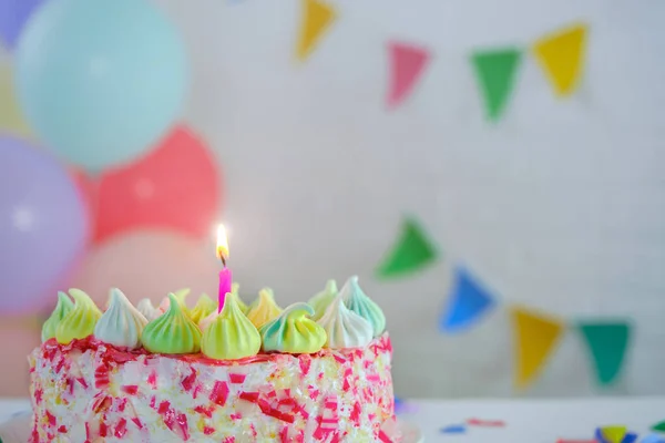 Balonların ve bayrakların arka planında yanan bir mum olan pasta. Kırmızı süslemeli pasta, çok renkli dekor, ev yapımı kekler. Konsept - tatil, doğum günü. kopyalama alanı, yatay fotoğraf.