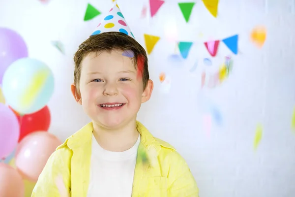 Ritratto di un bel ragazzo felice di 4-5 anni in un'atmosfera festosa, sullo sfondo di palloncini e bandiere triangolari multicolori. Concetto - vacanza, compleanno, partito. Foto orizzontale. — Foto Stock