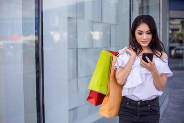 Asyalı güzel, mutlu, neşeli bir genç kadın portresi. İnternetten alışveriş yapmak için akıllı telefon taksitlerini kullanıyor.