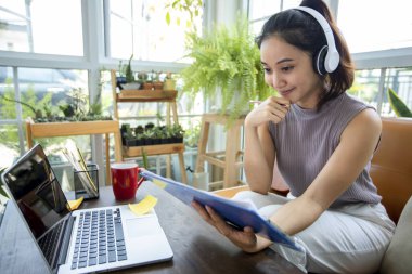 Asyalı iş kadınları defter bilgisayarları kullanıyor ve online toplantılarda kulaklık takıyor ve evden çalışıyorlar..