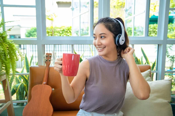 ヘッドフォンを着用し ノートパソコンやデジタルタブレットを使用しているアジアの女性自宅で音楽や歌を聴き リラックスした日にコーヒーを飲む — ストック写真