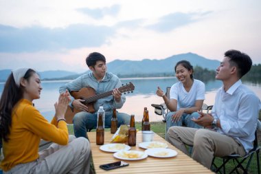Mutlu Asyalı arkadaş grubu gitar çalıp şarkı söylüyor kamp yapıyor ve bira içiyor.