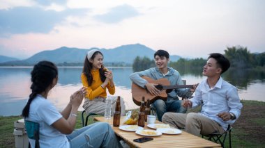Mutlu Asyalı arkadaş grubu gitar çalıp şarkı söylüyor kamp yapıyor ve bira içiyor.