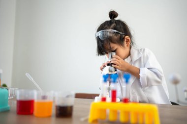 Laboratuvar önlüklü Asyalı çocuklar, laboratuarda bir bilim deneyi için mikroskop kullanıyorlar.