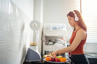 Sporcu kadın, kulaklıkla müzik dinlerken evdeki meyvelerden meyve püresi yapıyor. Yaşam tarzı kavramları.