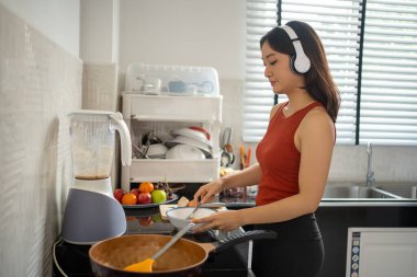 Güzel genç bir kadın evde mutfakta yemek pişirirken kulaklıkla müzik dinliyor - yaşam tarzı kavramları