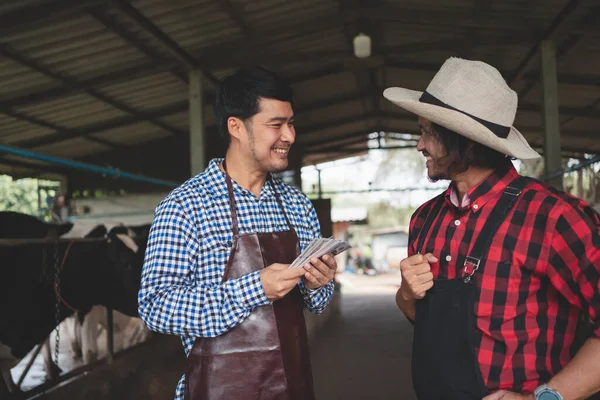 Male workers pay money and shake hands with farmers on the dairy farm.Agriculture industry, farming and animal husbandry concept ,Cow on dairy farm eating hay. Cowshed ,small business