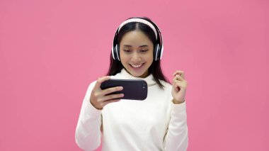 Asian women smiling and listening and singing the music with headphones on a pink studio background