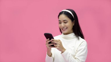 Tabletle gülümseyen ve cep telefonu kullanan Asyalı bir kadın izole edilmiş pembe arka planda online alışveriş için heyecanlı..