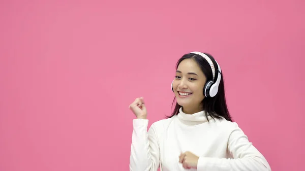 亚洲女人笑着 带着耳机在粉红的录音室里听着音乐 — 图库照片