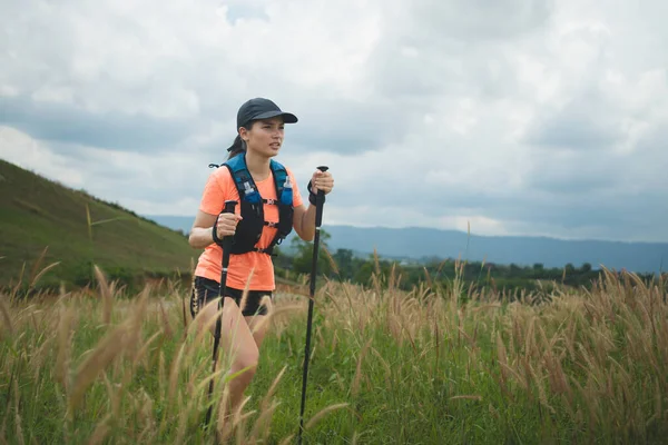 Young women active trail running across a meadow on a grassy trail high in the mountains in the afternoon with trekking pole