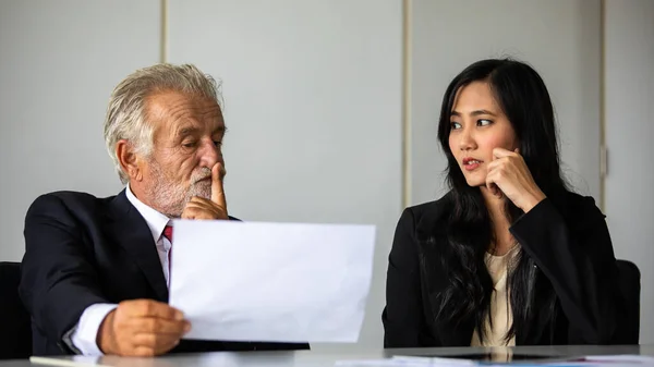 elderly Businessman and business woman sitting in a meeting and checking documents and notebooks on a desk in a meeting room.
