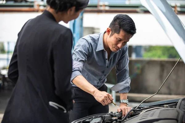 Businessman helping to check and fix a broken woman\'s car on the side of the road