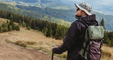 Sırt çantası ve yürüyüş sopalarıyla dağlarda yürüyen yürüyüşçü genç adam.