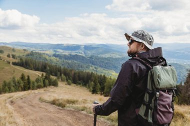 Sırt çantası ve yürüyüş sopalarıyla dağlarda yürüyen yürüyüşçü genç adam.