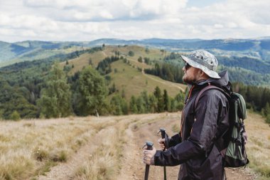 Sırt çantası ve yürüyüş sopalarıyla dağlarda yürüyen yürüyüşçü genç adam.