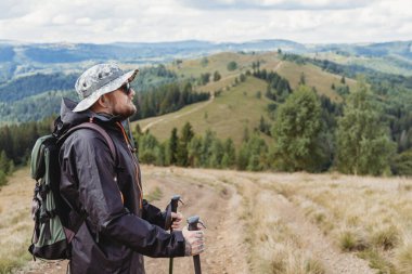 Sırt çantası ve yürüyüş sopalarıyla dağlarda yürüyen yürüyüşçü genç adam.