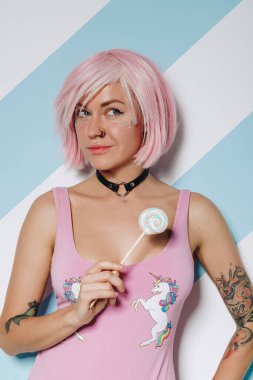 Pembe saç stili ve güzel makyajlı seksi genç kadın elinde renkli lolipop şekeri tutuyor.