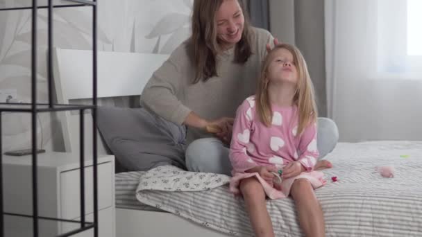 Egy gyönyörű anya fésüli a szőke, kusza haját egy kislánynak otthon. — Stock videók