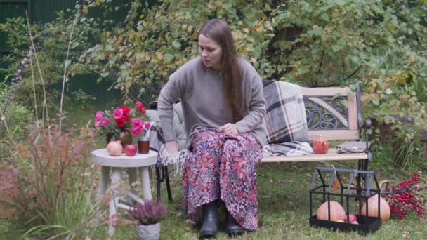 En smuk kvinde i efteråret i parken udgør for en fotograf på en bænk – Stock-video