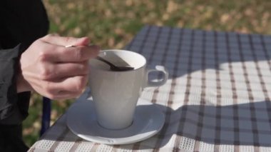 Dışardaki bir masada bir içecek bardağının yakın çekimi, bir kadın sonbaharda bir sokak kafesinde çay kaşığıyla çaya şekeri karıştırıyor..